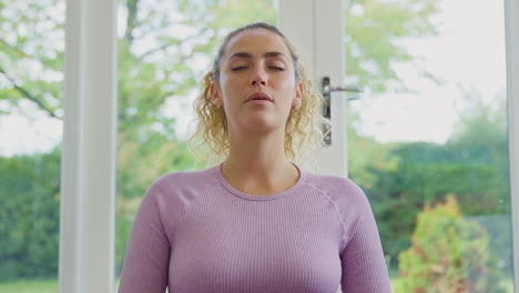 portrait of smiling young woman sitting on mat at home in yoga position meditating