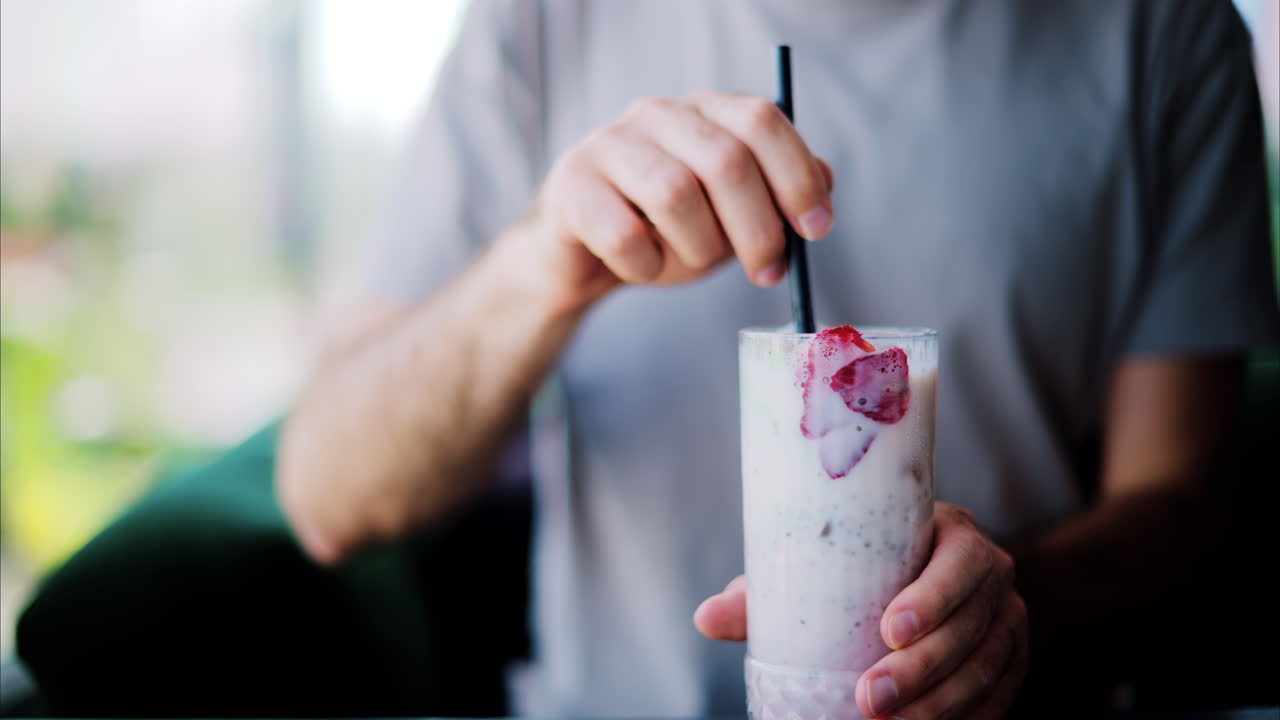 Man mixing a strawberry drink with a black straw at a restaurant