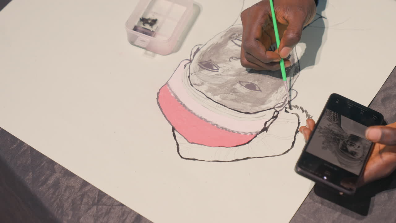 Black portrait layering artist applying wash gentle gray tones sculpt cheek and brow, phone reference nearby, water tray and green brush visible, tabletop lighting, teaching cadence and observational