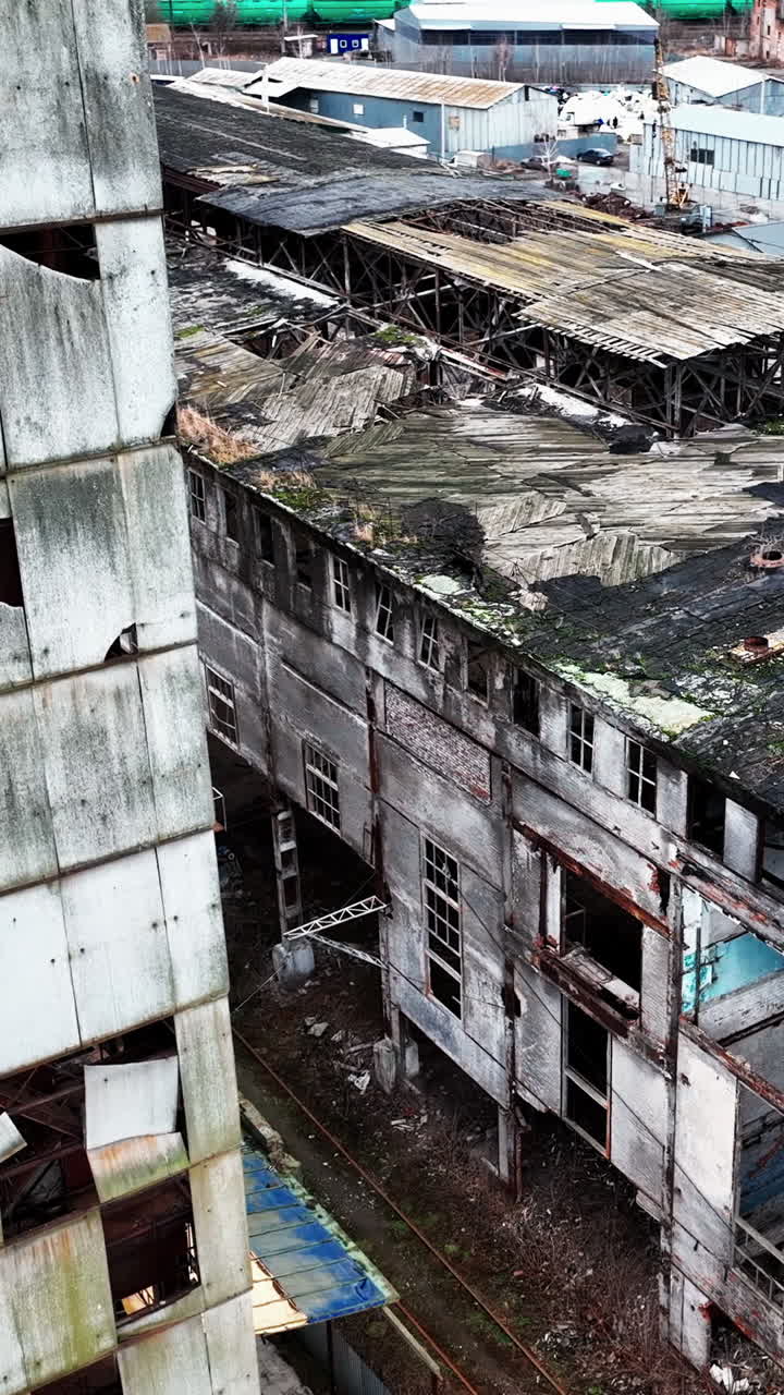 Decayed exterior of an old chemical factory complex. Grey ruined walls and roofs of the buildings from aerial perspective. Vertical video