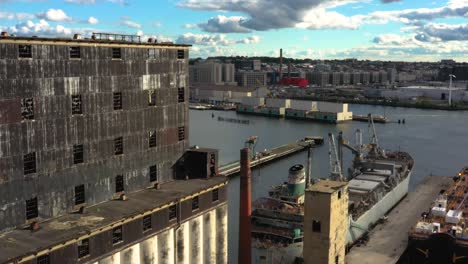 aerial pull back next to massive grain terminal and old ship in an industrial harbor in brooklyn new york city