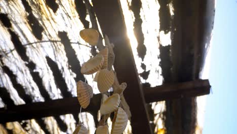 Slow-motion-shot-of-a-bunch-of-seashells-hanging-from-a-patio-roof-with-sun-flares