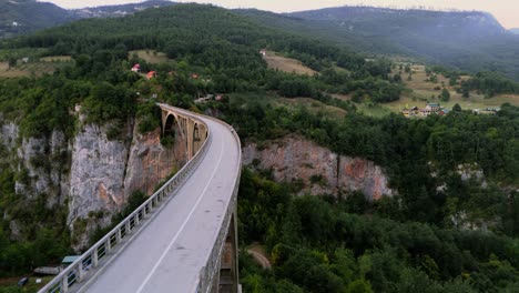 volando cerca sobre el puente durdevica tara revelando el paisaje bosque verde y montañas de montenegro cruzando el río tapa al anochecer en verano mientras los coches pasan y cruzan tapa