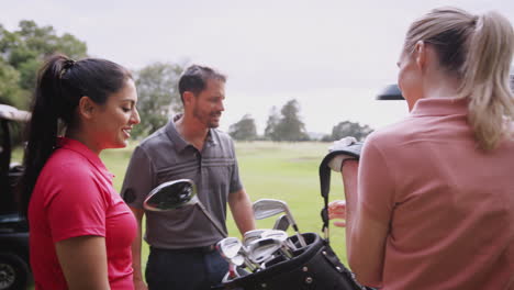 group of male and female golfers standing by golf buggy on course and choosing clubs