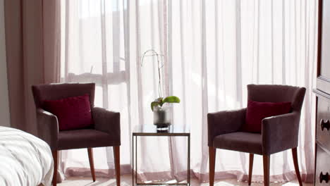 Dos-Sillones-Marrones-Con-Cojines-Rojos-Están-Colocados-Junto-A-Una-Ventana-Con-Cortinas-Transparentes