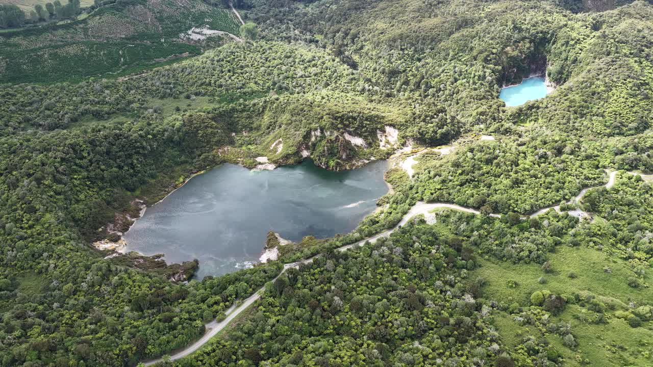Órbita de dron en sentido horario sobre lagos geotérmicos en el Valle Volcánico de Waimangu, Nueva Zelanda, con impresionantes árboles forestales y paisaje volcánico.