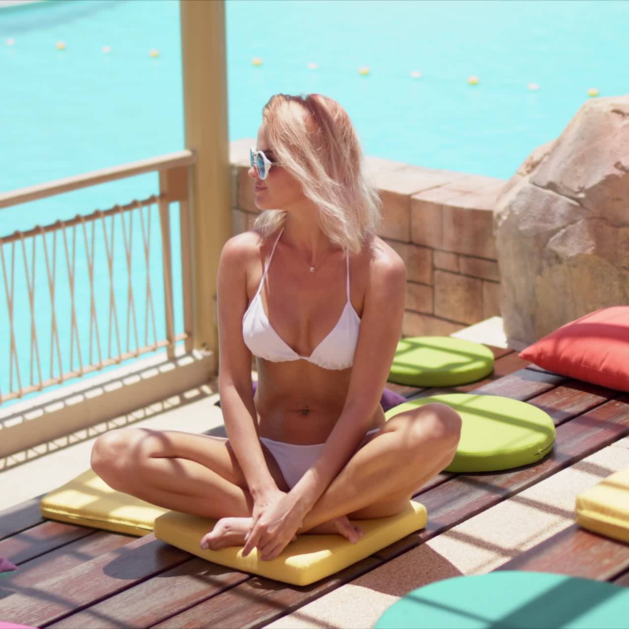 elegante mujer bronceada sentada con las piernas cruzadas sobre almohadas coloridas en la terraza abierta