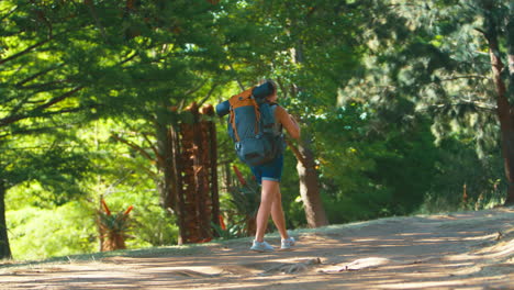 woman with backpack waving as she sets off on vacation hiking through countryside