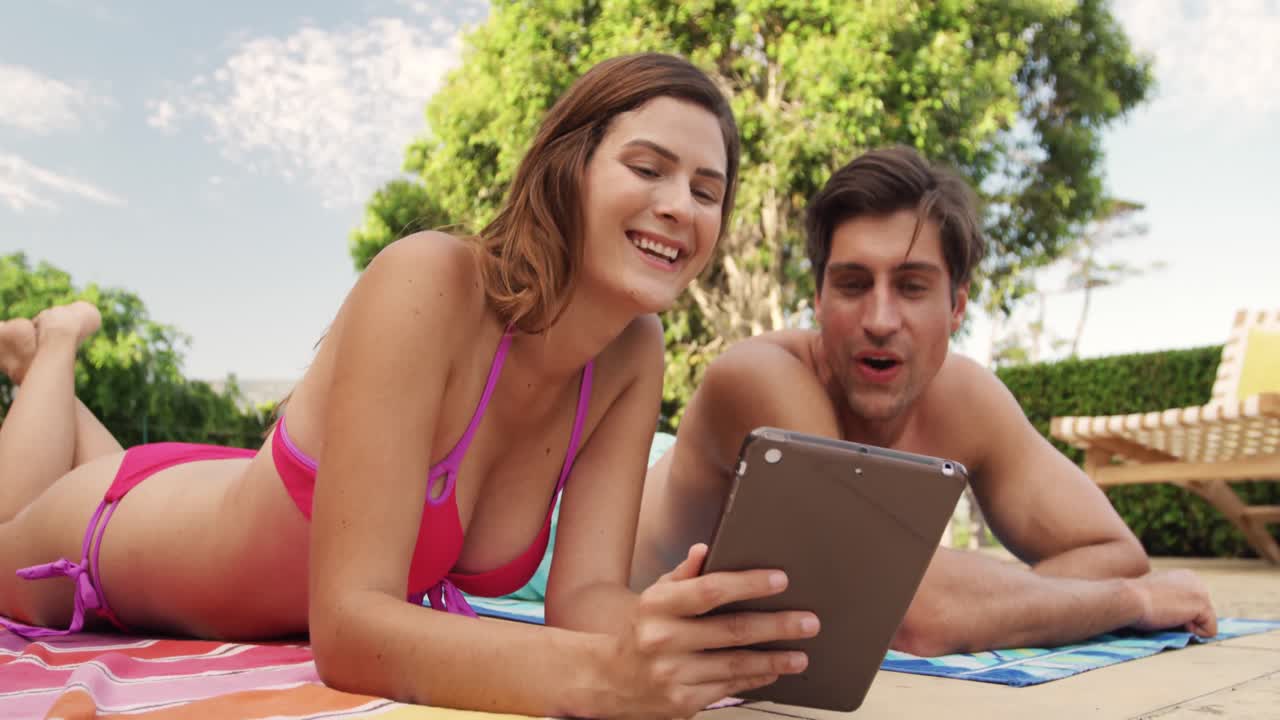 una feliz pareja caucásica usando una tableta digital cerca de la piscina