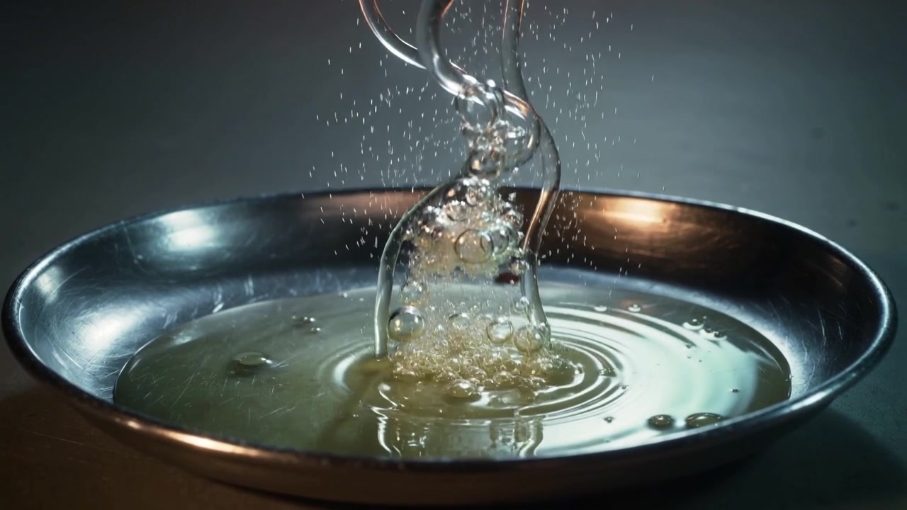 Versamento di liquido viscoso dall'alto che forma una colonna con sottili rivoli, bolle in una ciotola di metallo in studio