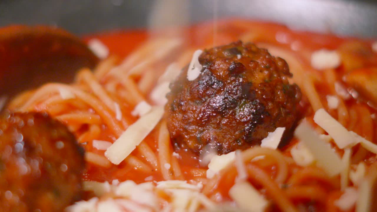 Close Up Slow Motion of Cheese Dropping onto Italian Meatballs with Spaghetti Pasta in Rich Tomato Passata Sauce. Homemade Cooking Food Footage.