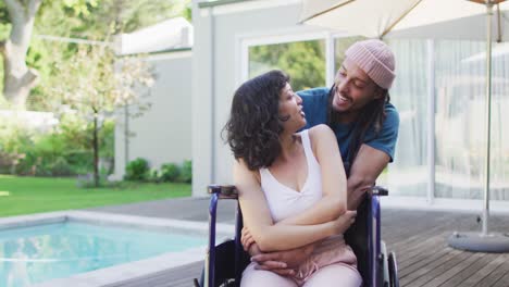 Happy-biracial-couple-embracing-in-garden,-woman-in-wheelchair,-man-with-dreadlocks