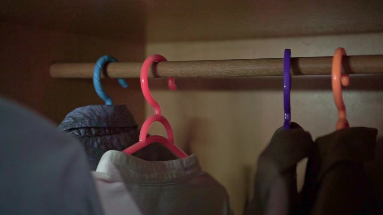 Mano eligiendo ropa de perchas coloridas en el armario. Metraje de estilo de vida interior, concepto de vestuario, moda y organización del hogar.