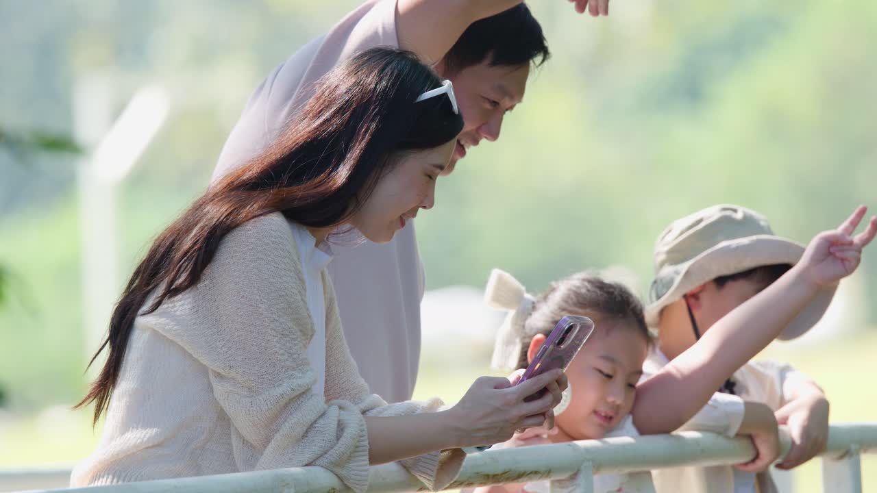 아시아 가족이 야외 여행 중에 손으로 하트 모양을 만들고 스마트폰을 보고 있어요.