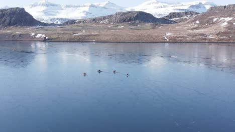 cuatro kayakistas en aguas tranquilas con superficie semi congelada en el fiordo de islandia