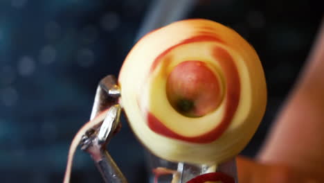 an out-of-focus person using a hand crank peeler to peel, core, and slice an organic, homegrown apple