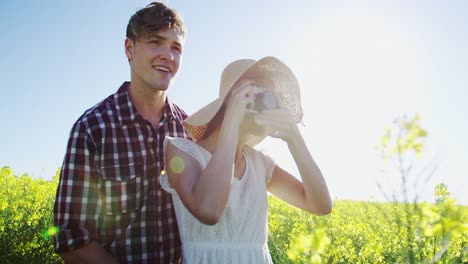 Pareja-Tomando-Fotografías-De-La-Cámara-En-El-Campo-De-Mostaza