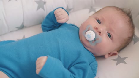 funny baby sucks dummy lying in soft sleeping cocoon at home