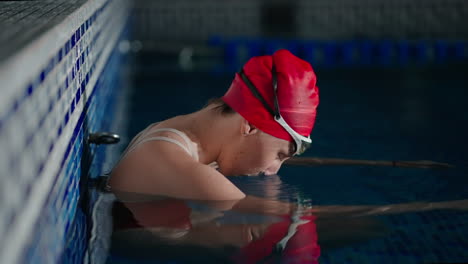 mujer con una gorra de natación roja y gafas preparándose para nadar en una piscina