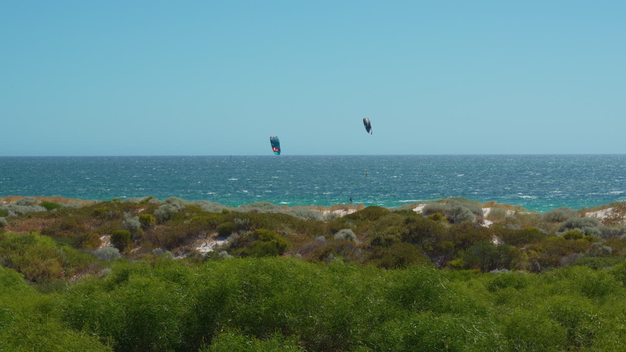 Kitesurfistas surfando as ondas na Praia de Mullaloo, Perth. Dia ensolarado, céu azul límpido, perspectiva dinâmica que cria o cenário perfeito para a aventura.