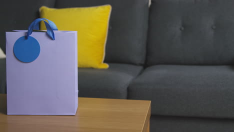 close up of man putting gift wrapped present in bag with tag on table in lounge at home