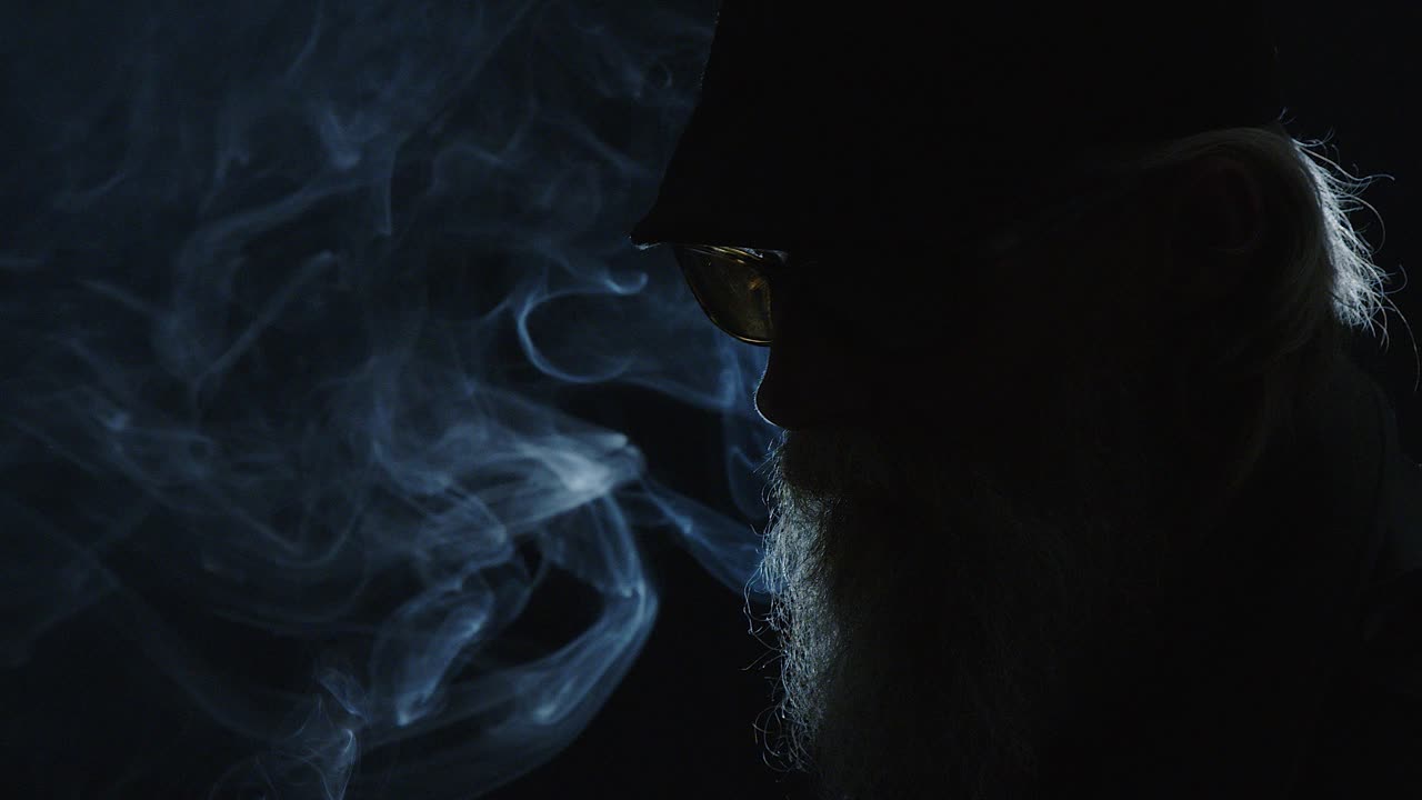 Cool, bearded man holds burnt match in smoky, dark jazz portrait