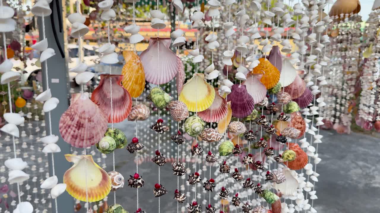 Handcrafted seashell mobiles gently move in daylight at a vibrant outdoor souvenir market stall