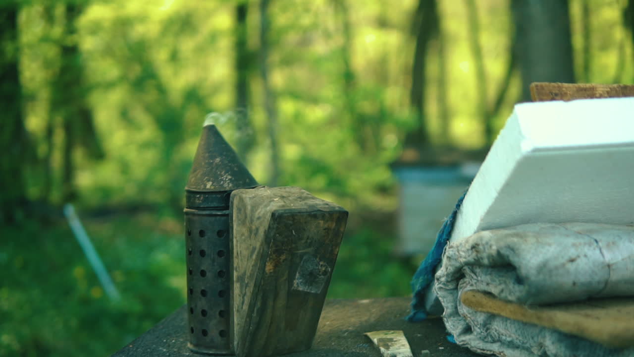 Imker-Smoker ruht auf dem Tisch, Rauch kommt aus der Düse und Bienen fliegen vorbei. Starre Aufnahme, Zeitlupe