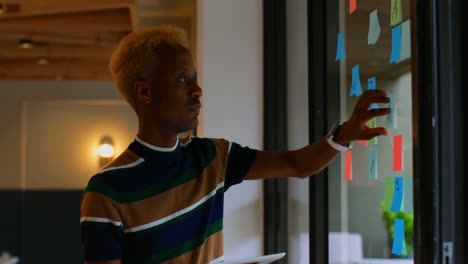 side view of young mixed race male executive looking at sticky note and working on digital tablet 4k