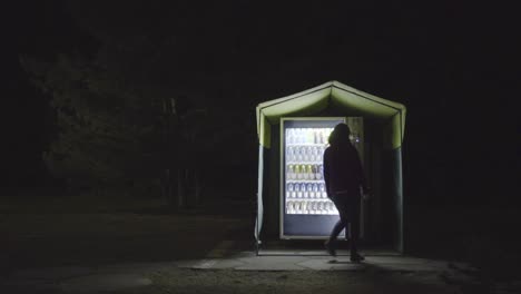 person walking past illuminated vending machine at night