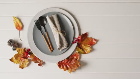 video of plate with cutlery and autumn decoration with leaves on white surface