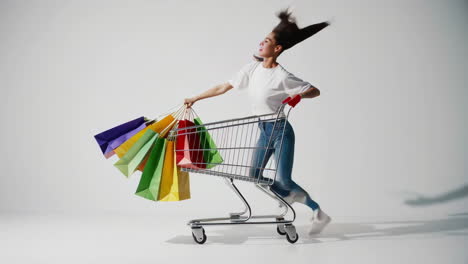 excited young woman pushing shopping cart with colorful bags