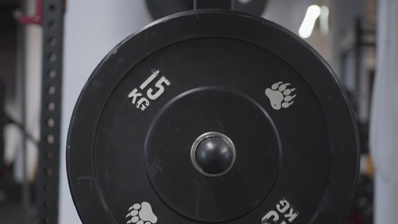 Slow motion close-up moves across black weight plates stored on an equipment rack inside a modern commercial gym.