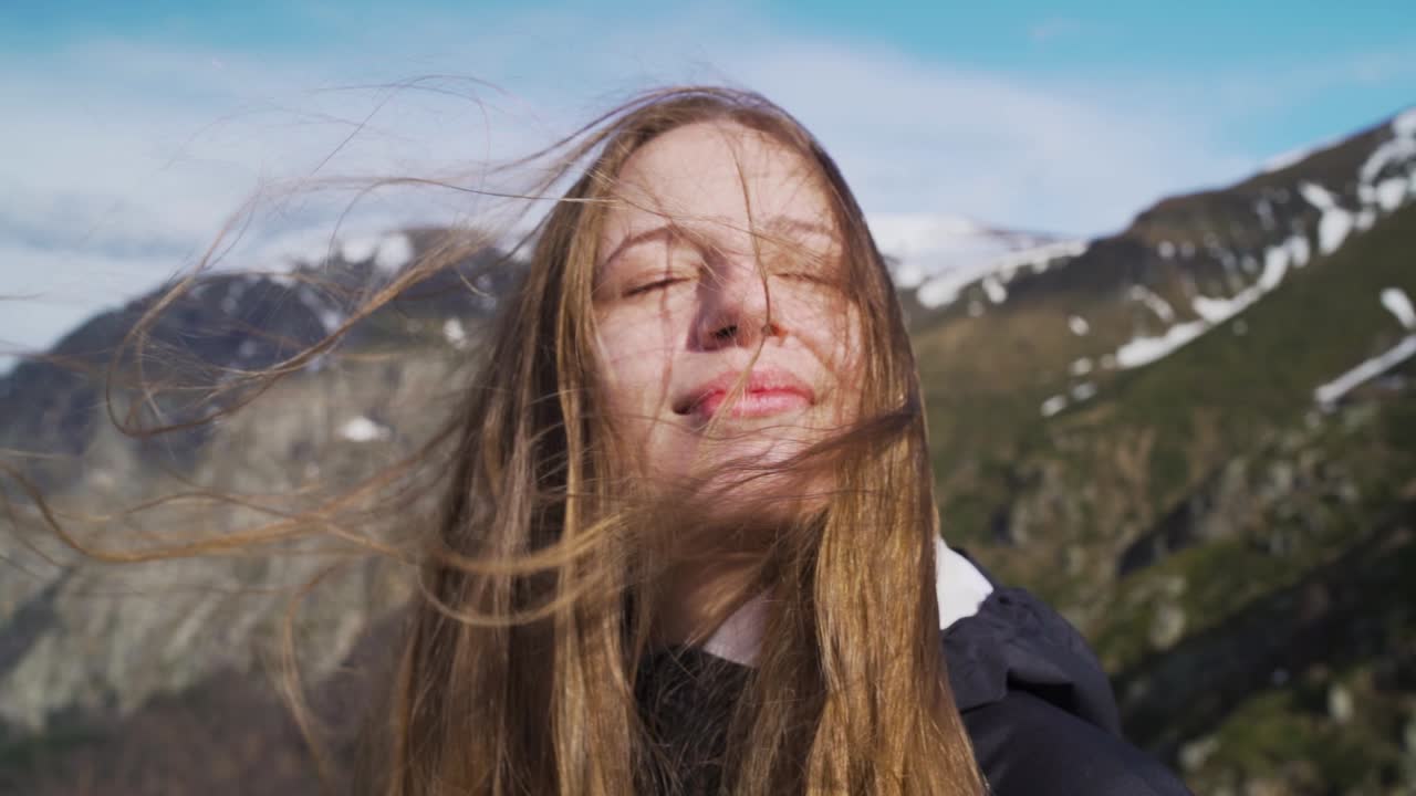 A woman stands smiling with wind-swept hair at the summit of Botev Peak in Stara Planina. The slow motion captures natural movement and emotion