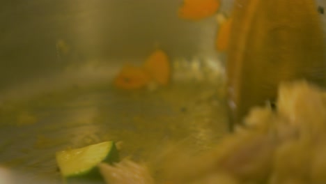 el cocinero mezcla pollo con calabacín y zanahorias en una olla de acero, haciendo ensalada de pasta, primer plano de mano
