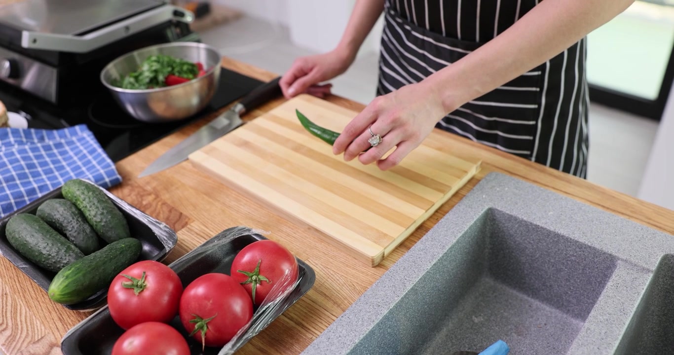 Mano di donna che mette un peperoncino verde su un tagliere di legno