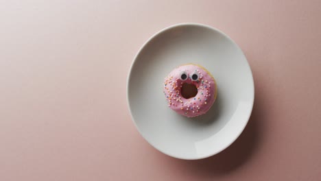 video of donut with icing on white plate over pink background