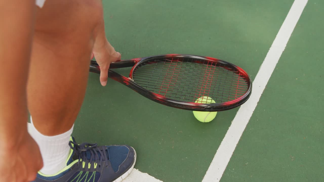 Someone picking up tennis racket and ball