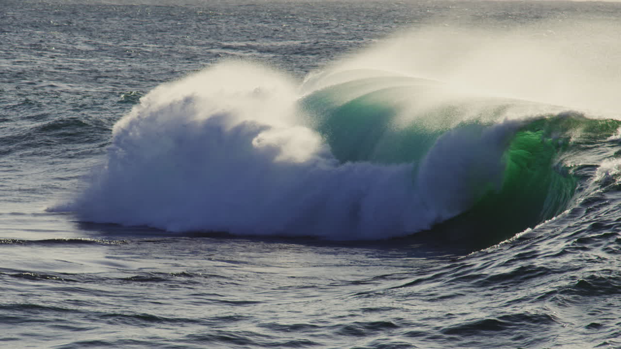 Mid-sized wave folds and crashes with whitewater under cloudy skies, moving toward camera