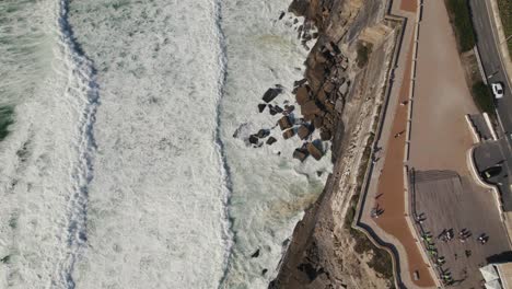 cinematic aerial top down dolly in shot of foamy waves hitting coastal rocky cliffs