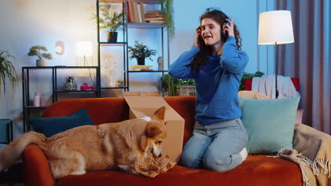 surprise young woman opening cardboard delivery box receives wireless headphones beside corgi dog