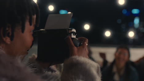 young-happy-friends-posing-for-photo-on-rooftop-at-night-enjoying-party-african-american-woman-photographing-reunion-gathering-using-polaroid-camera