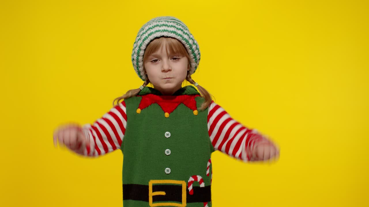 Nespokojená holčička v kostýmu vánočního skřítka pomocníka Santa Clause drží palec dolů a ukazuje gesto nesouhlasu.