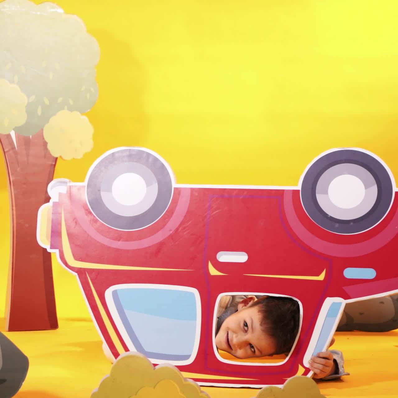Little boy with a red car in the studio. Yellow background. Bright scenery.