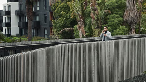 hombre de traje hablando por teléfono mientras caminaba por un puente de la ciudad.