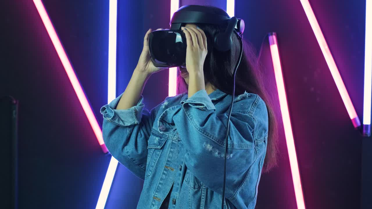una giovane donna indossa un auricolare vr, si guarda intorno e si chiede come sia fantastico nella realtà virtuale. casco di realtà virtuale sullo sfondo di illuminazione a colori