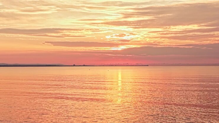 Sunset over the ocean with clouds and reflections on the water at a calm evening near the shore
