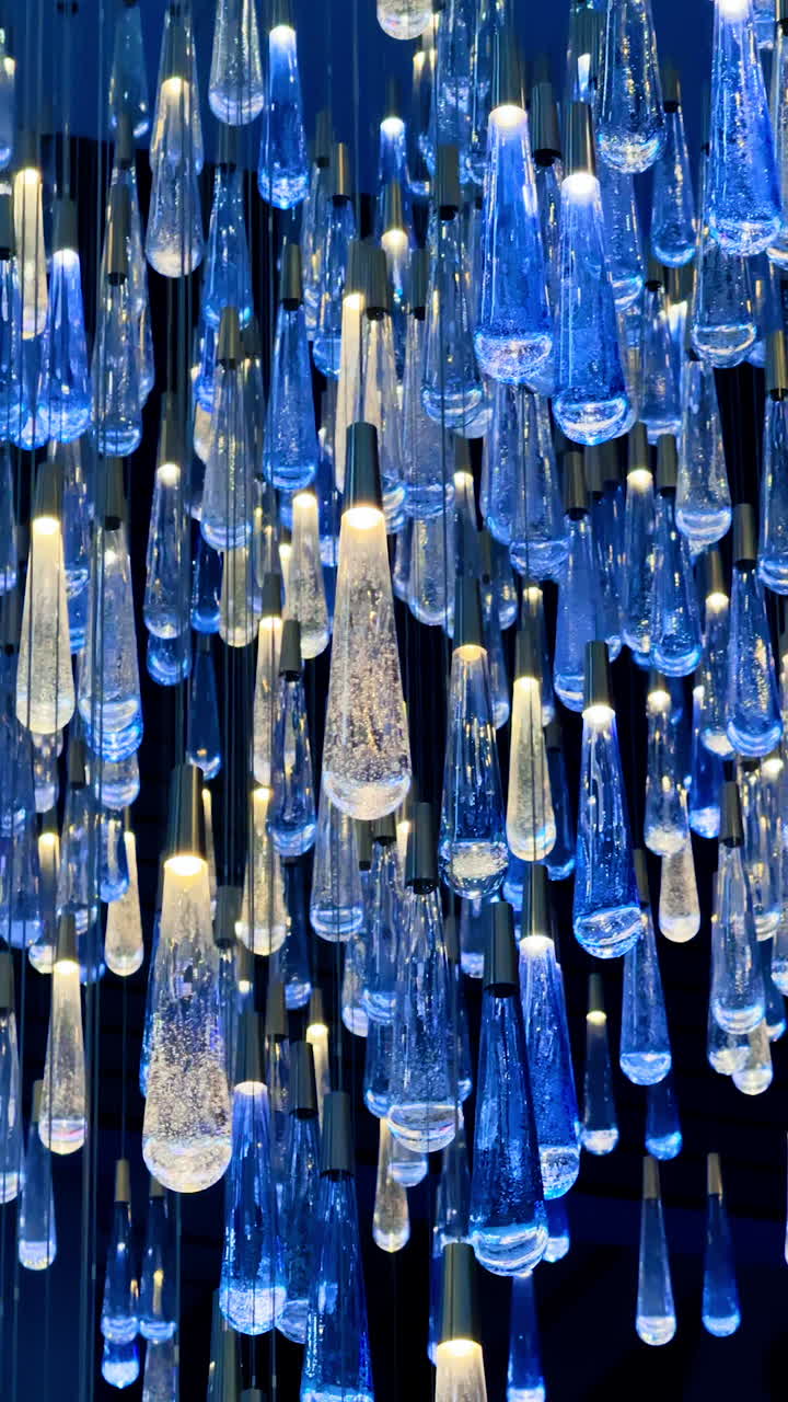 Multiple unusually-shaped light bulbs hanging from the ceiling. Blue and white lamps for decoration. Vertical video.