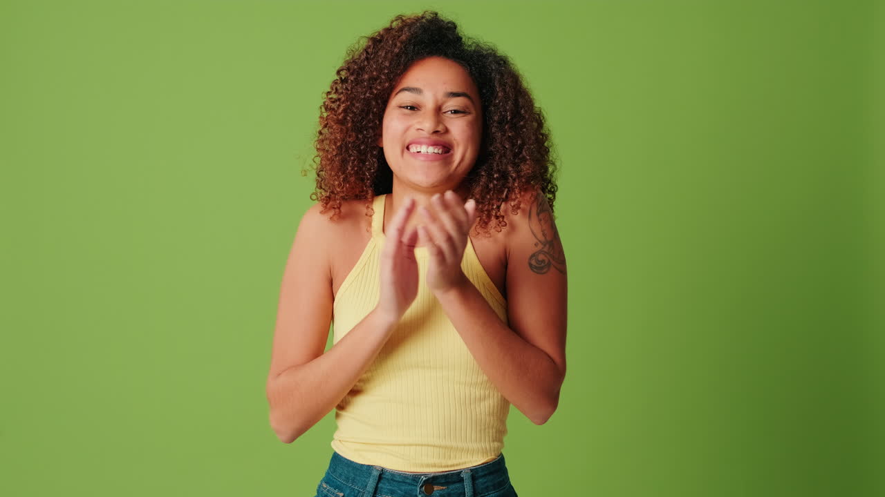 Giovane donna afroamericana felice che batte le mani su sfondo verde