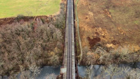 aerial, top down drone video footage of a train bridge viaduct running over a valley and stream in the appalachain mountains during early spring on a cloud day